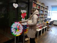 Widok na wnętrze biblioteki. Czytelnik stoi obok koła do losowania.