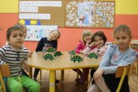 Grupa dzieci przy stoliku z papierowymi dinozaurami