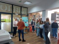 Grupa uczniów wraz z nauczycielem podczas zwiedzania wystawy w bibliotece