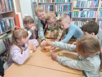 Dzieci z przy stolikach podczas zajęć w bibliotece