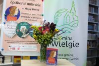 Książka na tle plakatu i baneru Gmina Wielgie